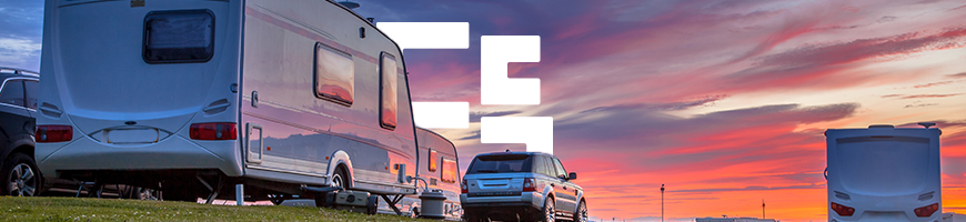 Caravans and a parked car on a grassy field at sunset.