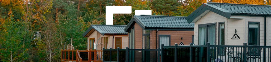 Row of three static caravans surrounded by green grass and autumn trees in the background.