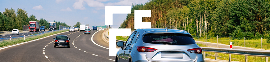 A silver car drives on a sunny motorway in Poland surrounded by green trees under a blue sky with fluffy clouds