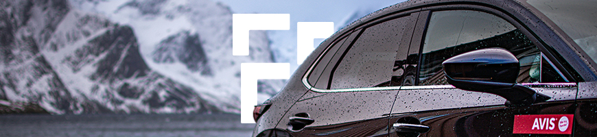 Black Avis hire car with water droplets on parked in front of snowy mountain
