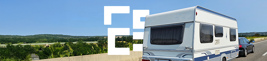 A car pulling a touring caravan down an empty road that is surrounded by greenery and is under a clear blue sky