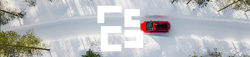 Aerial view of a bright red car driving down a snowy road surrounded by tall green pine trees