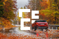 Colorful autumn leaves scattered across a winding road with a red Range Rover driving down it