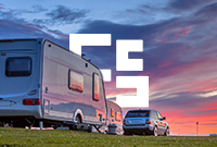 Caravans and a parked car on a grassy field at sunset.