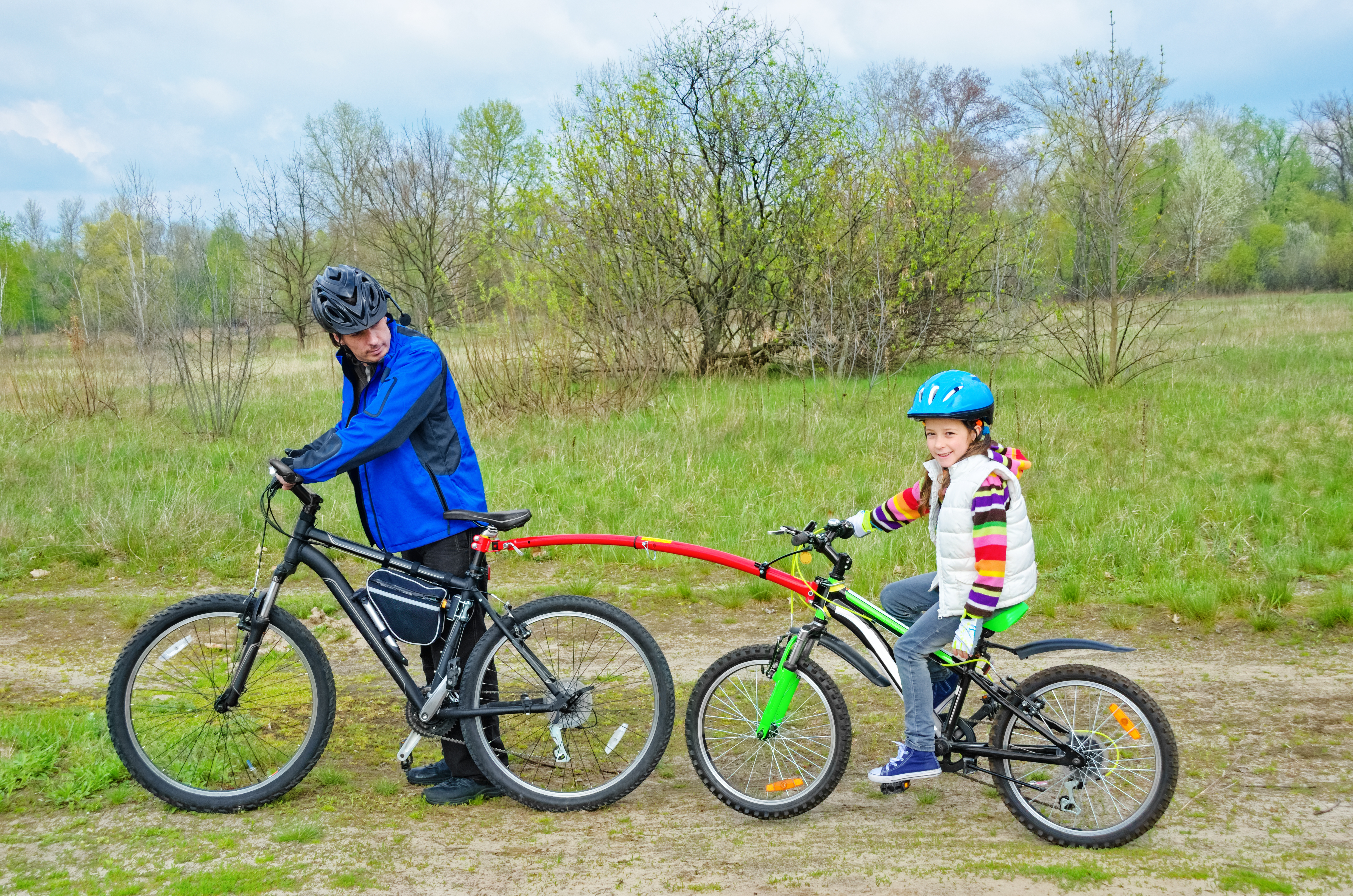 Father teaching daughter to cycle with a bike tow bar