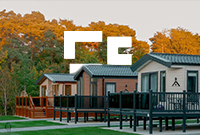 Row of three static caravans surrounded by green grass and autumn trees in the background.