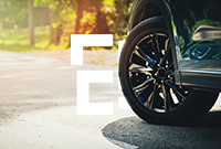Close-up of a black car's front wheel on a sunny road