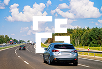 A silver car drives on a sunny motorway in Poland surrounded by green trees under a blue sky with fluffy clouds
