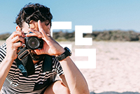 Close up of man wearing stripy tshirt looking through his viewfinder and adjusting his focus on a beach