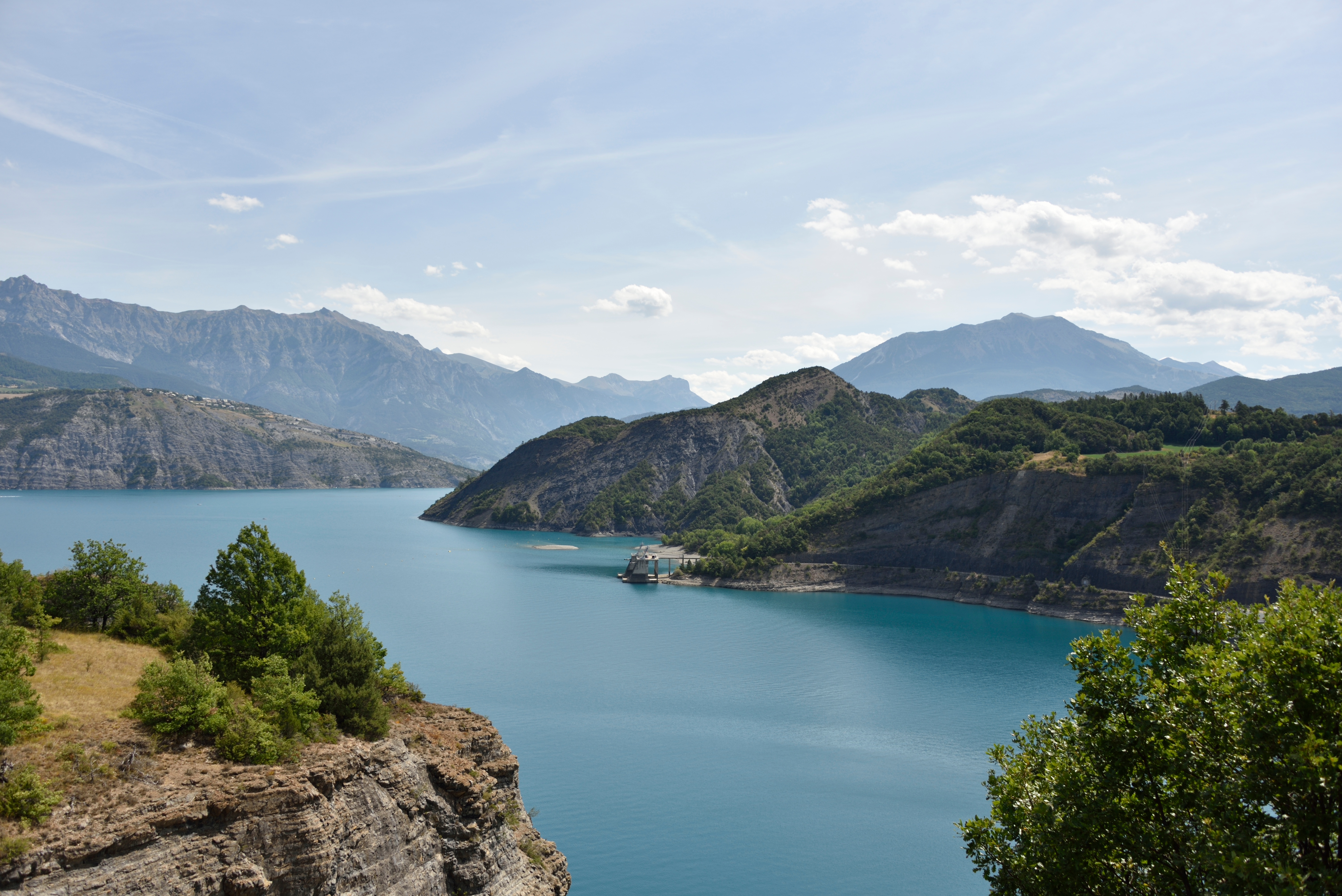 Lac de Serre-Ponçon under a clear sky reflecting light and surrounded by distant land