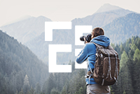 Man wearing a blue hoodie uses a large DSLR camera to photograph a mountain landscape