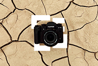 Black DSLR laying on sand coloured cracked ground