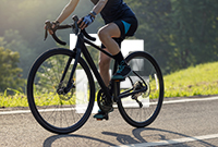 A person riding a bicycle along a road surrounded by greenery and a clear blue sky