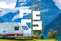 A touring caravan parked in front of a mountain landscape under a clear blue sky