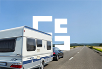 A car pulling a touring caravan down an empty road that is surrounded by greenery and is under a clear blue sky