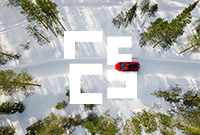 Aerial view of a bright red car driving down a snowy road surrounded by tall green pine trees.
